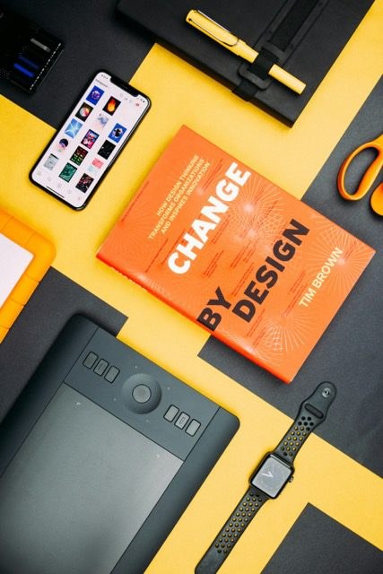 A flat-lay of a designer's desk with a phone, a design book, a graphics tablet, and an Apple Watch.